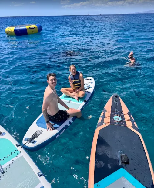 Two smiling guests on a stand-up paddleboard next to the ocean trampoline in turquoise water